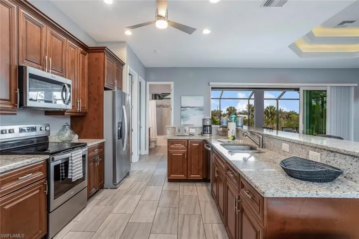Kitchen featuring stainless steel appliances, a ceiling fan, light stone countertops, wood finish cabinets, and recessed lighting
