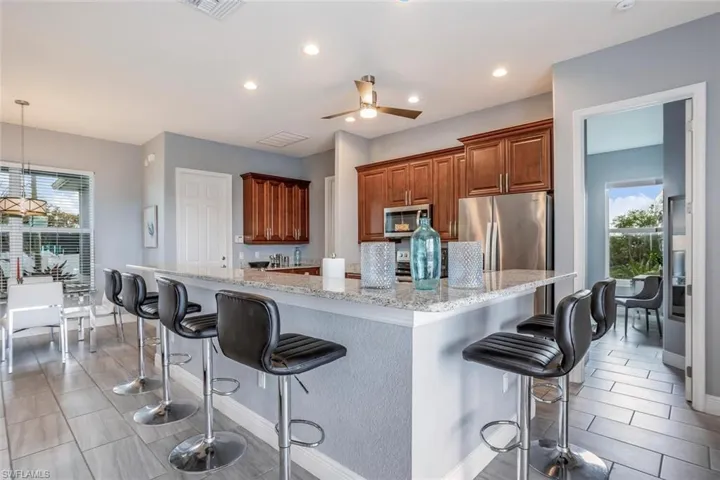 Kitchen featuring healthy amount of natural light, a kitchen bar, light stone counters, and wood finish cabinetry