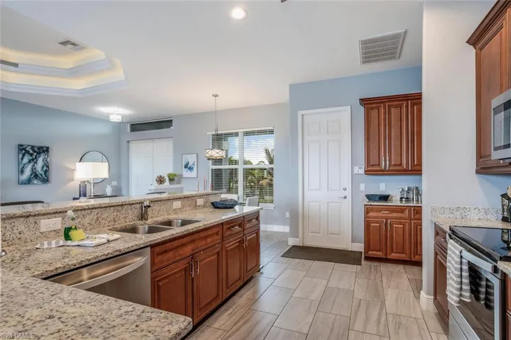 Kitchen featuring stainless steel appliances, wood finish cabinetry, light stone countertops, pendant lighting, and a raised ceiling