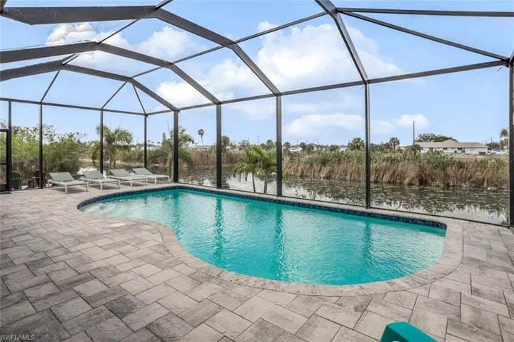 Swimming pool featuring a sunroom, a water view, glass enclosure, and a patio area
