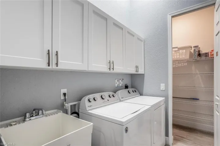 Laundry room featuring a textured wall, cabinet space, washing machine and dryer, and light wood-style flooring