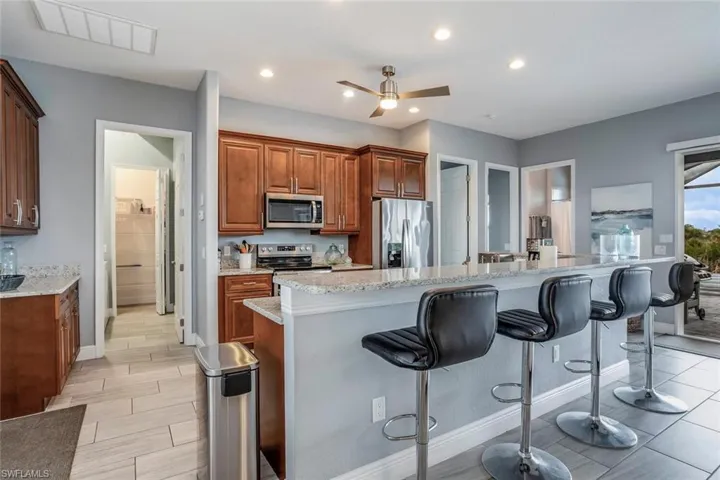 Kitchen featuring wood finish cabinetry, a ceiling fan, stainless steel appliances, a breakfast bar area, and light stone countertops