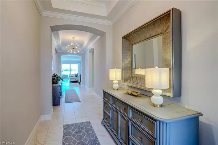 Hallway with baseboards, crown molding, a raised ceiling, arched walkways, and marble finish floor