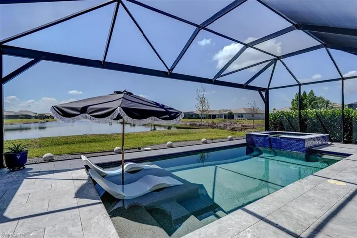 View of swimming pool with a patio area, a yard, a water view, a pool with connected hot tub, and a lanai