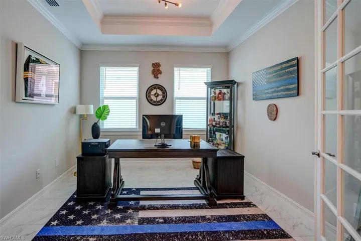 Home office with a raised ceiling, marble finish floor, and ornamental molding