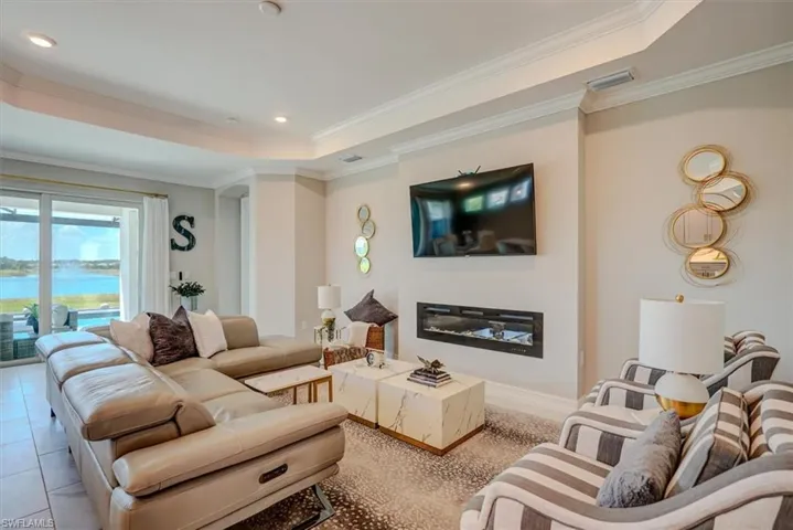 Living area featuring a tray ceiling, ornamental molding, a glass covered fireplace, and visible vents
