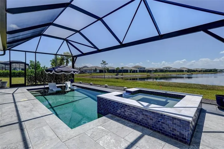Pool featuring a patio area, an in ground hot tub, glass enclosure, and a water view