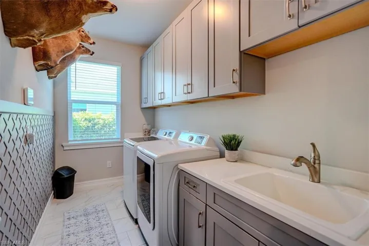 Clothes washing area with baseboards, a sink, cabinet space, marble finish floor, and washing machine and clothes dryer