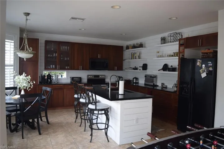 Gourmet kitchen with rich wood-finish cabinetry, black countertops, and a white shiplap accent wall