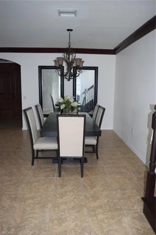 Formal dining area featuring a bronze chandelier with amber glass shades, decorative ceiling trim, and large format tile flooring