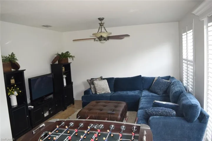 Living area featuring white walls, wood-finish flooring, and a ceiling fan with integrated lighting