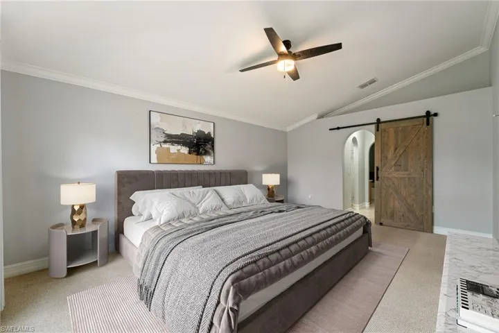 Carpeted bedroom featuring a barn door, ornamental molding, lofted ceiling, and a ceiling fan