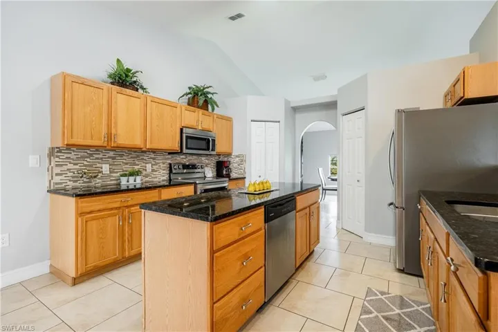 Kitchen featuring arched walkways, light tile patterned floors, stainless steel appliances, dark stone countertops, and a center island