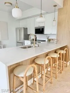 Kitchen featuring white cabinetry, kitchen peninsula, stainless steel appliances, a kitchen breakfast bar, and decorative light fixtures
