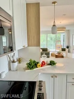 Kitchen with stovetop, white cabinetry, light stone counters, and pendant lighting