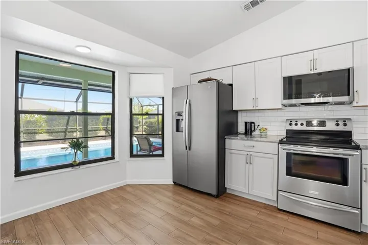 Kitchen with appliances with stainless steel finishes, lofted ceiling, tasteful backsplash, white cabinetry, and wood finish floors