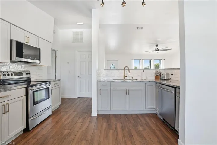 Kitchen featuring stainless steel appliances, tasteful backsplash, light stone countertops, dark wood-style floors, and ceiling fan