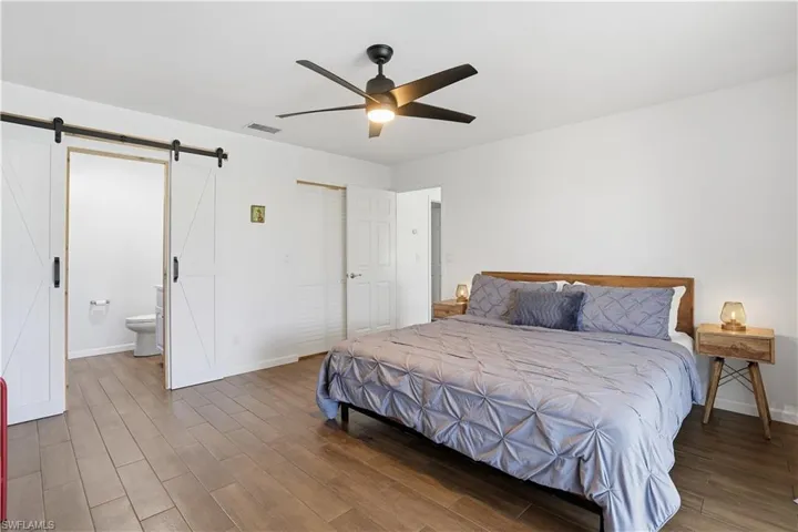 Bedroom with wood finished floors, ceiling fan, ensuite bath, and a barn door