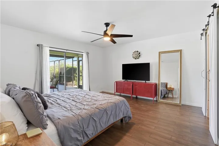 Bedroom featuring wood finished floors, a barn door, access to outside, and ceiling fan