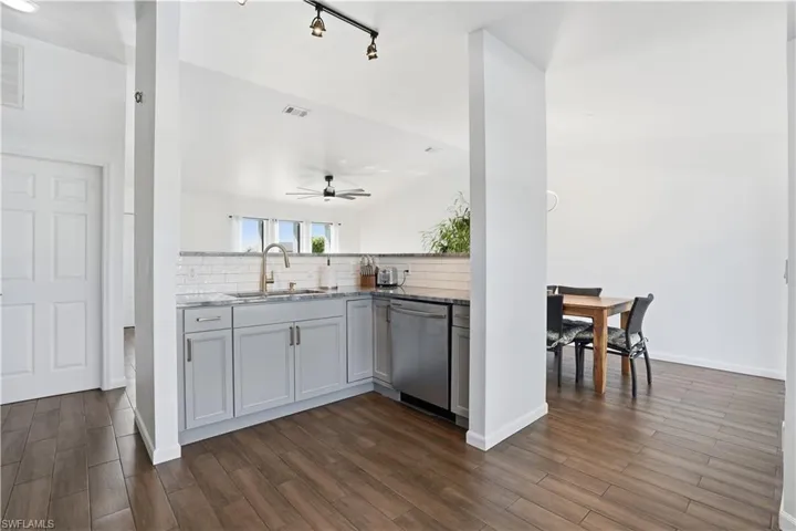 Kitchen featuring light stone countertops, dark wood finished floors, stainless steel dishwasher, gray cabinets, and backsplash