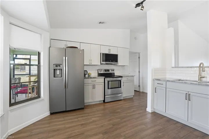 Kitchen featuring appliances with stainless steel finishes, tasteful backsplash, vaulted ceiling, light stone countertops, and dark wood-style flooring