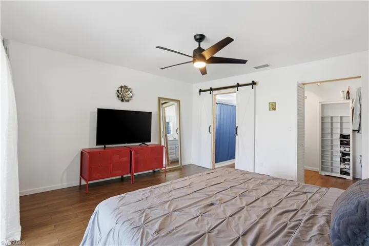 Bedroom with hardwood / wood-style flooring, a barn door, a ceiling fan, and ensuite bathroom