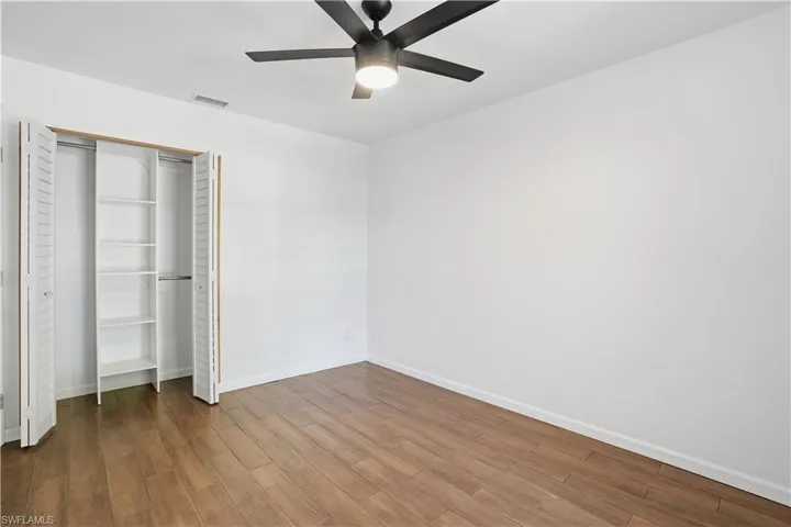 Unfurnished bedroom with dark wood-type flooring, a closet, and a ceiling fan