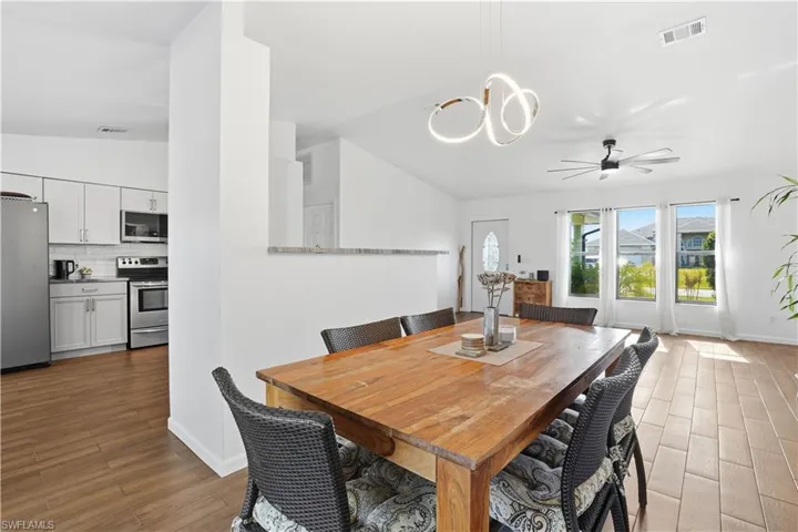 Dining space with light wood-style flooring, a ceiling fan, a chandelier, and vaulted ceiling