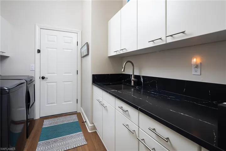 Kitchen with washing machine and dryer, sink, white cabinets, and wood-type flooring