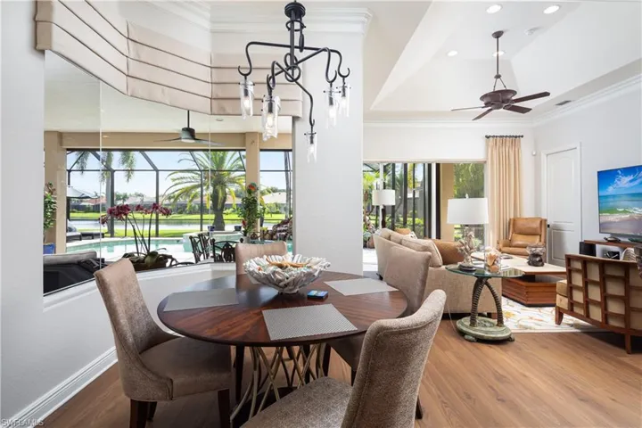 Dining space featuring ceiling fan with notable chandelier, a tray ceiling, hardwood / wood-style flooring, and ornamental molding
