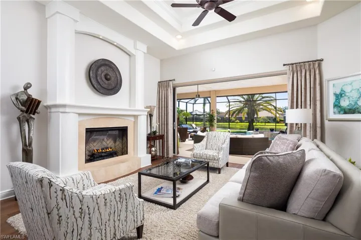 Living room with hardwood / wood-style flooring, a fireplace, ceiling fan, and a raised ceiling