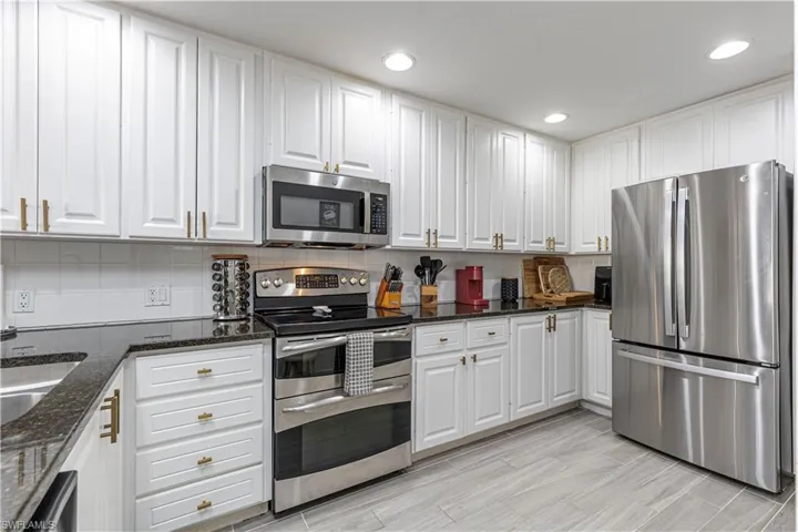 Kitchen featuring stainless steel appliances, white cabinets, dark stone countertops, recessed lighting, and decorative backsplash
