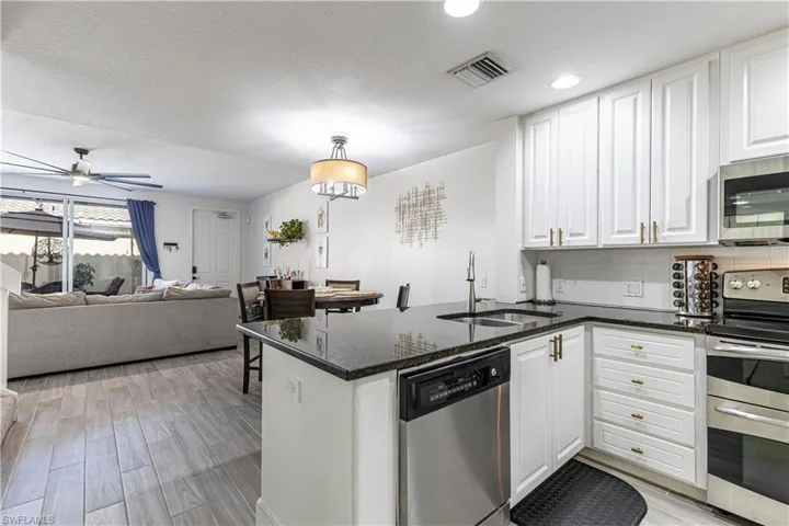 Kitchen with a peninsula, stainless steel appliances, dark stone countertops, white cabinetry, and light wood finished floors