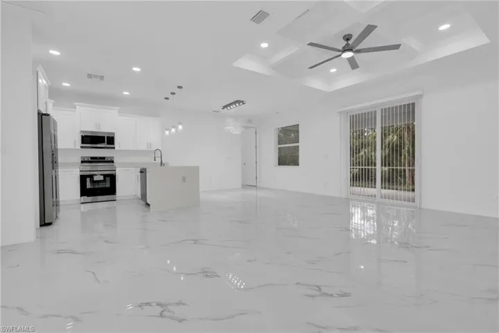 Unfurnished living room featuring coffered ceiling, recessed lighting, light marble finish floors, a ceiling fan, and beamed ceiling
