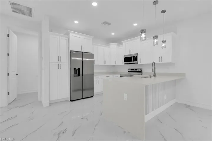 Kitchen with white cabinetry, appliances with stainless steel finishes, recessed lighting, a peninsula, and hanging light fixtures