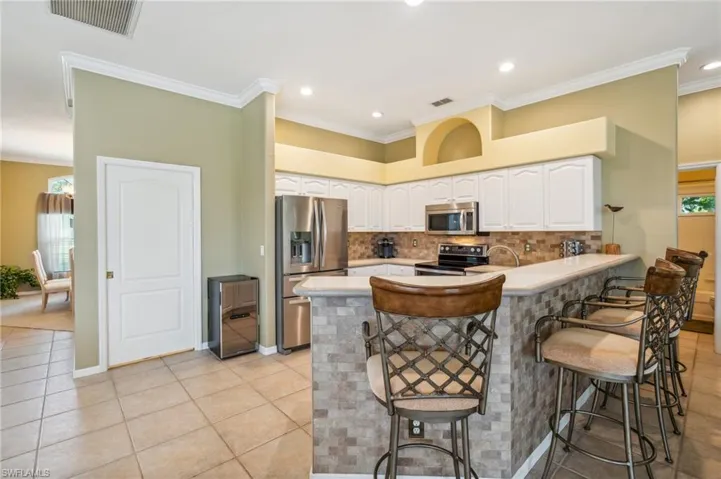 Kitchen featuring appliances with stainless steel finishes, white cabinetry, kitchen peninsula, a kitchen bar, and ornamental molding