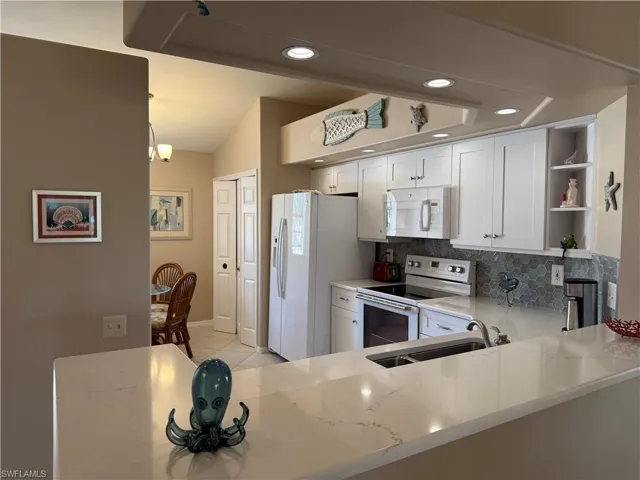 Kitchen with white appliances, light stone countertops, kitchen peninsula, sink, and tasteful backsplash