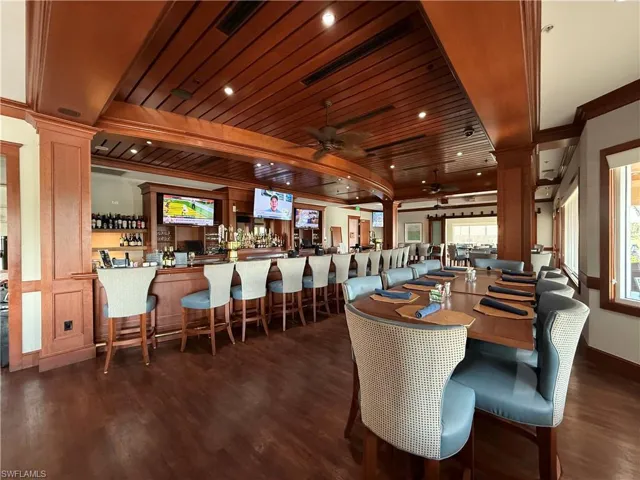 Dining space featuring wooden ceiling, indoor bar, ceiling fan, dark wood-type flooring, and decorative columns