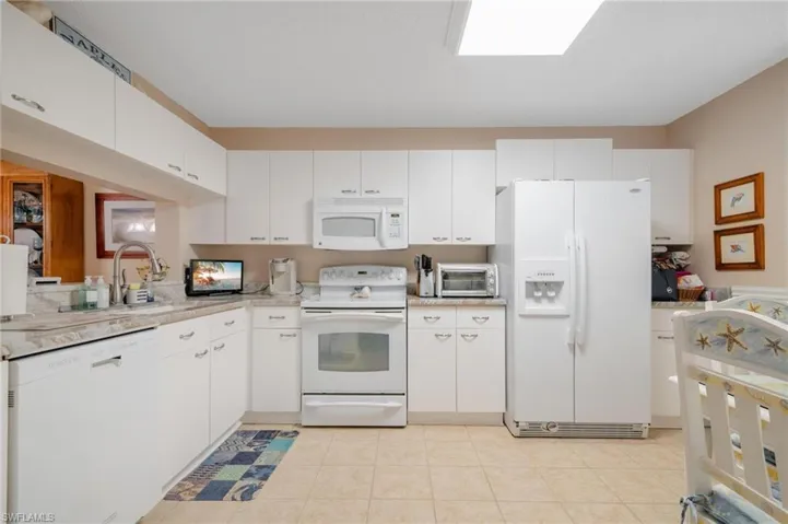 Kitchen featuring light tile patterned flooring, sink, white appliances, and white cabinets