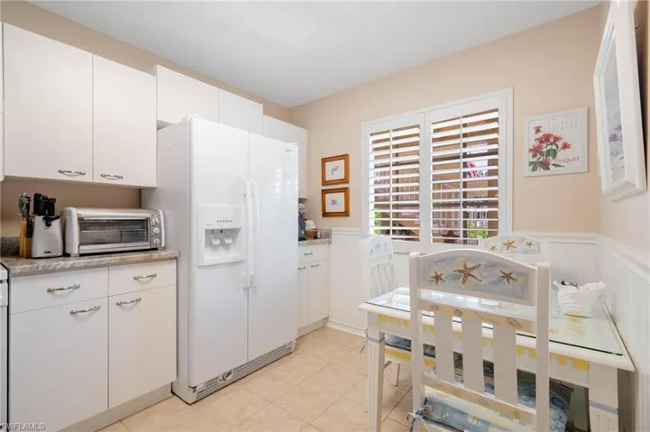 Kitchen with light tile patterned floors, white fridge with ice dispenser, and white cabinets