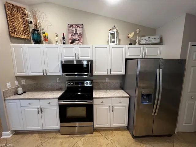 Kitchen with stainless steel appliances, white cabinetry, and light tile patterned flooring