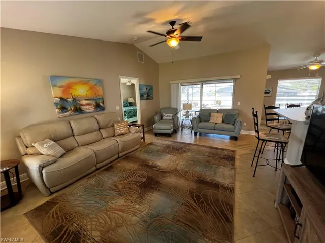 Living room with a ceiling fan, vaulted ceiling, light tile patterned floors, and healthy amount of natural light