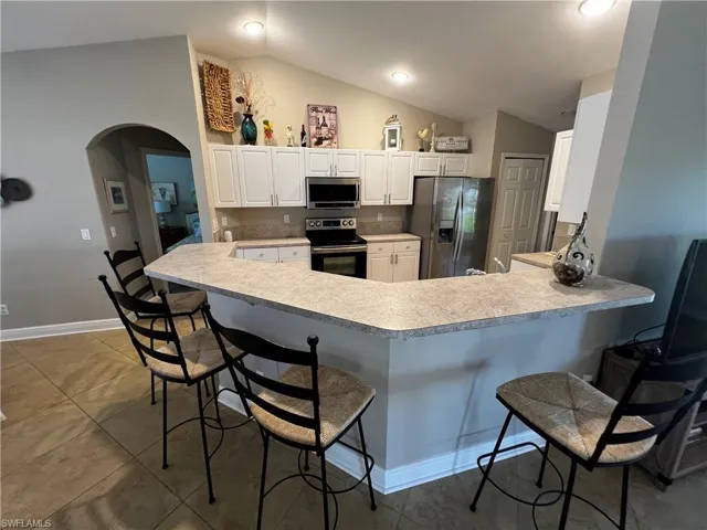 Kitchen featuring a breakfast bar area, arched walkways, lofted ceiling, stainless steel appliances, and light countertops