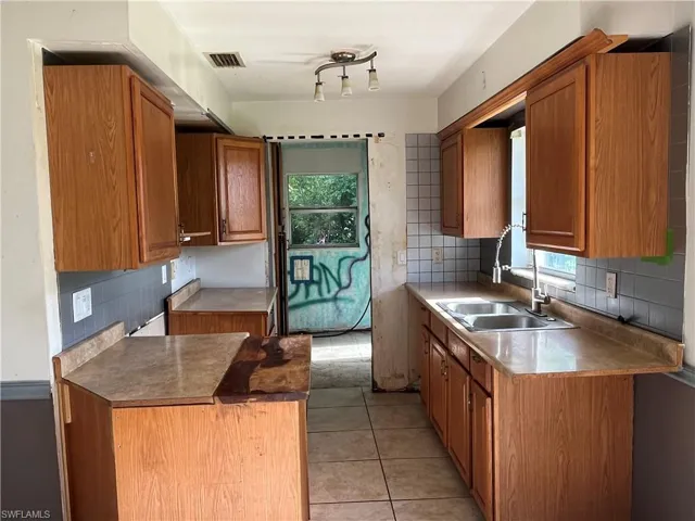 Kitchen with light tile patterned flooring, backsplash, track lighting, and a healthy amount of sunlight