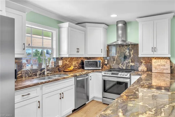 Kitchen with dark stone counters, stainless steel appliances, white cabinets, decorative backsplash, and recessed lighting