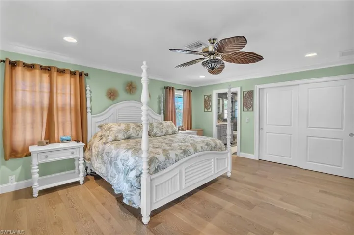 Bedroom with light wood-style floors, a closet, ensuite bath, ornamental molding, and recessed lighting
