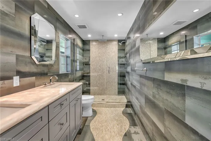 Full bath featuring tile walls, double vanity, a stall shower, and recessed lighting