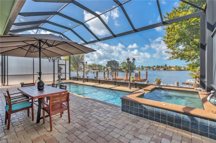 Relaxing pool / spa featuring a sunroom, a patio area, a lanai, outdoor dining space, and a water view