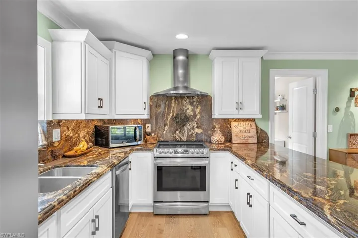 Kitchen with stainless steel appliances, dark stone counters, white cabinets, crown molding, and light wood-style floors