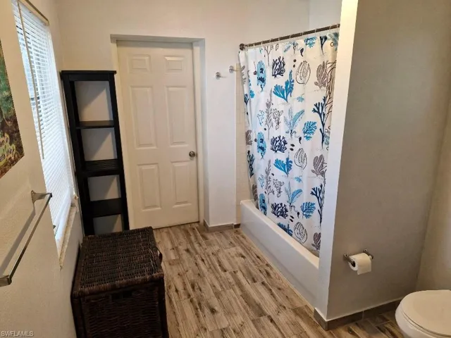 Bathroom featuring shower / bath combo, wood finished floors, toilet, and baseboards